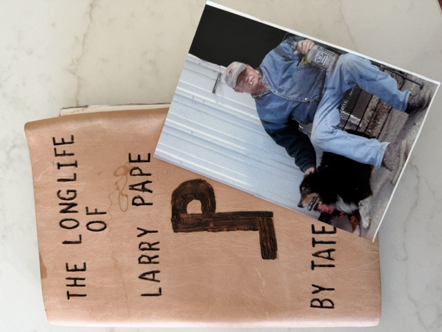 A handmade book titled The Long Life of Larry Pape, resting beside a photograph of Larry Pape